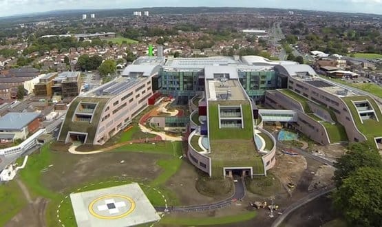 Modern hospital building with green rooftop gardens and surrounding landscape.